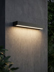 AI Studio Photo - Standing facing the camera, natural confident posture, arms relaxed at sides, front view, full body visible. CAMERA SHOT: A medium shot focusing on the wall lamp, showcasing its clean lines and the warm light it casts on the wall. [Half body styled]