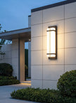 AI Studio Photo - Standing facing the camera, natural confident posture, arms relaxed at sides, front view, full body visible. CAMERA SHOT: Medium shot showcasing the lamp mounted on a wall, with a hint of the surrounding architecture and landscaping. [Full body]