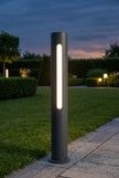 AI Studio Photo - Standing facing the camera, natural confident posture, arms relaxed at sides, front view, full body visible. CAMERA SHOT: A medium shot focusing on the bollard light, showcasing its full height and the integrated light strip. [Half body styled]