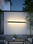 AI Studio Photo - Standing facing the camera, natural confident posture, arms relaxed at sides, front view, full body visible. CAMERA SHOT: A medium shot focusing on the wall lamp and its illuminated effect, with a hint of the surrounding outdoor patio setting. [Half body styled]